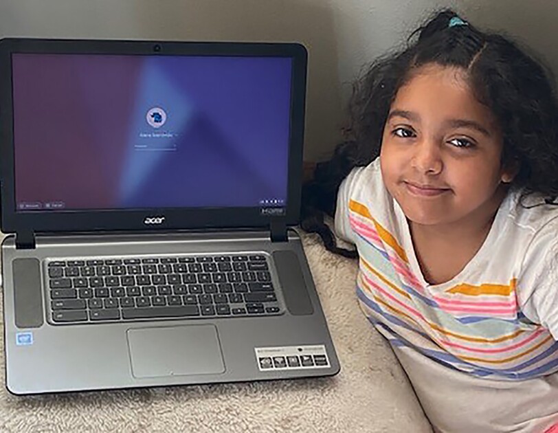 An elementary age student sits with their laptop computer in their home