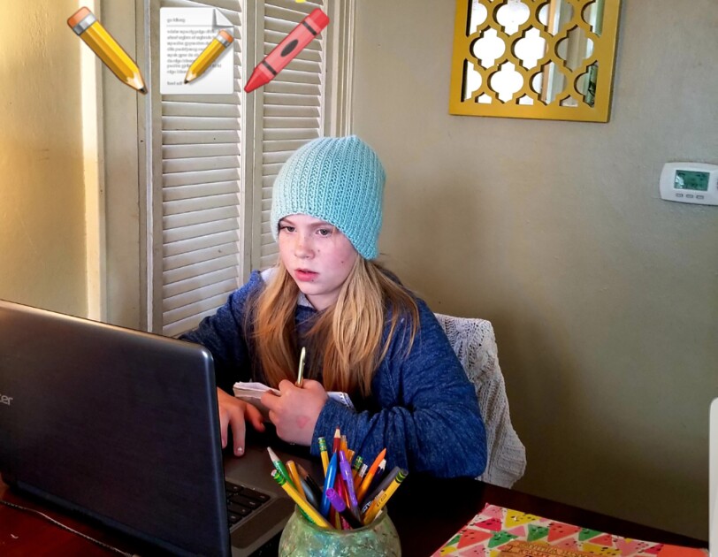 An elementary age student sits with their laptop computer in their home