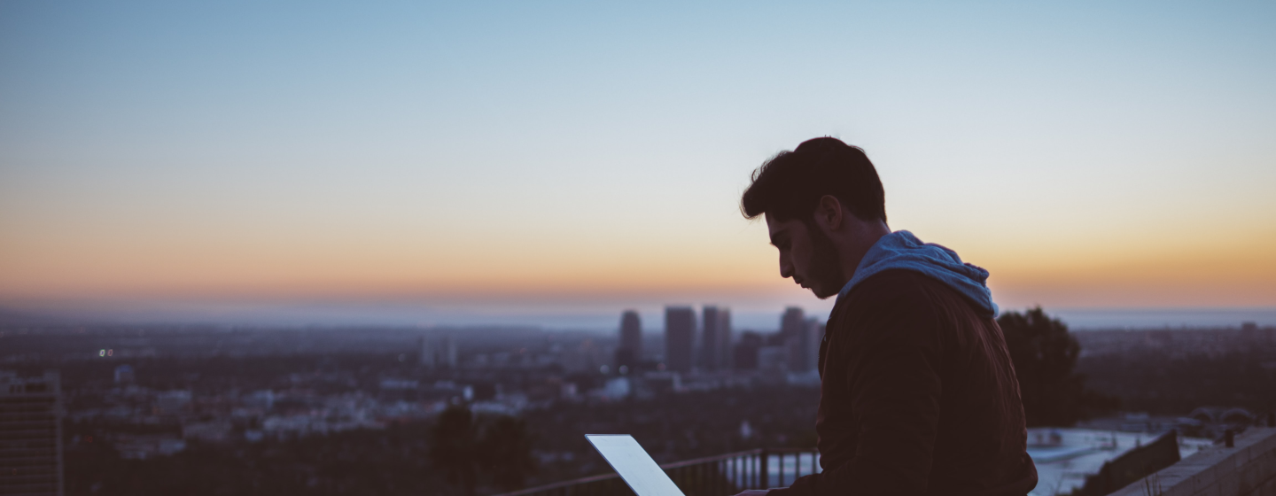 Man sat on a wall typing on his laptop