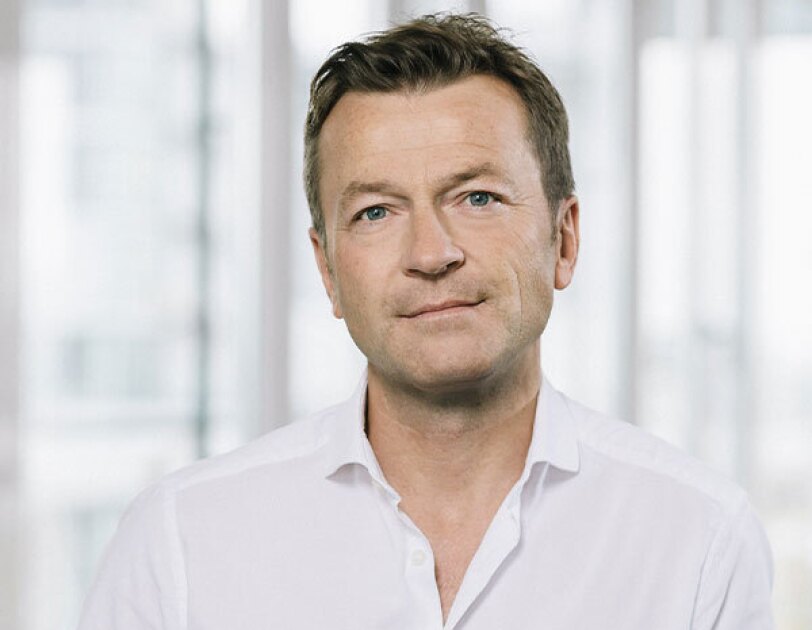 Ein Mann mit weißem Hemd und dunklen Haaren lächelt in die Kamera.