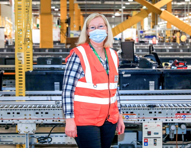 Carole Wee standing in front of a conveyor belt in a fulfilment centre.