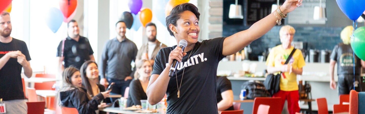 A woman Amazonian in a black t-shirt that says Equality points during a speech.