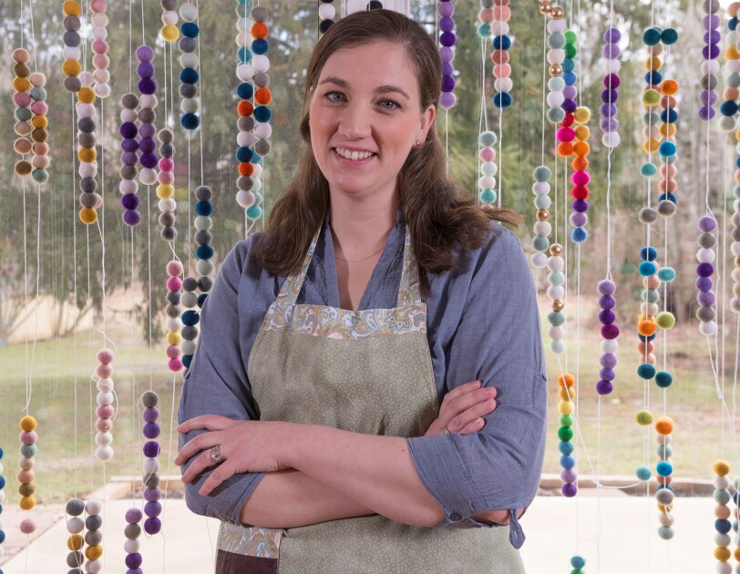 Amazon Handmade seller posing in a photograph in front of the felted wool ball garlands she makes and sells.