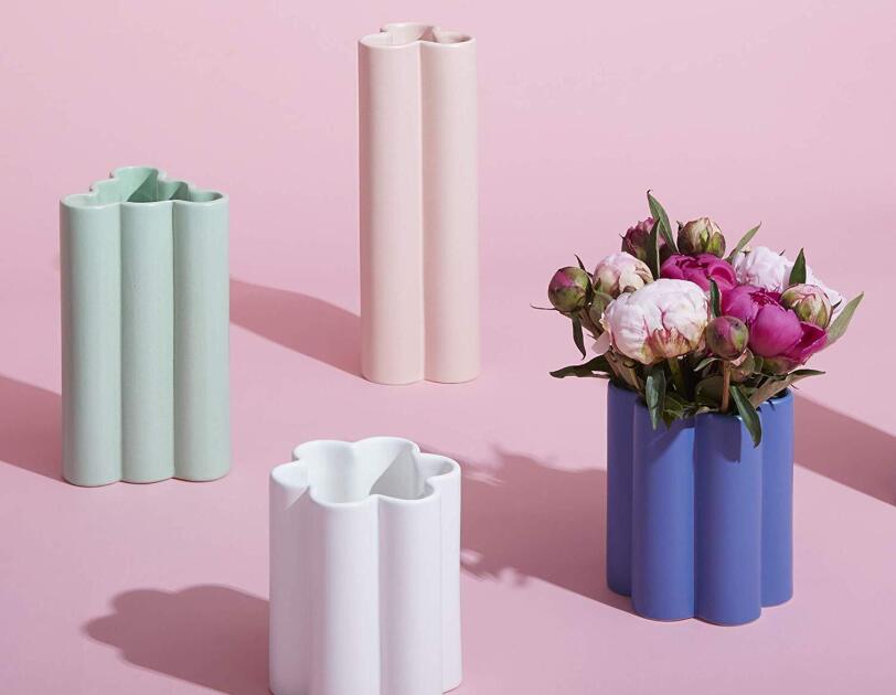 Four shaped vases in varying heights and width. The tallest vase is pink and has a three-petal shape, aqua is slightly smaller and has a bubbly triangular shape, blue is slightly smaller and a six-petal shape, white is shortest and also has a six-petal shape.