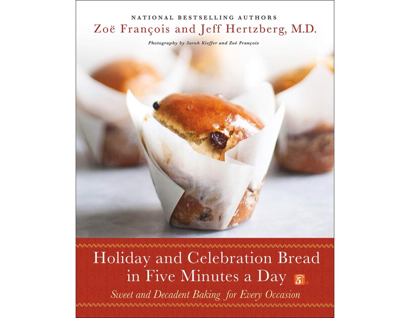 A holiday cook book with a celebration bread in parchment paper wrap, in front of other bakery treats.