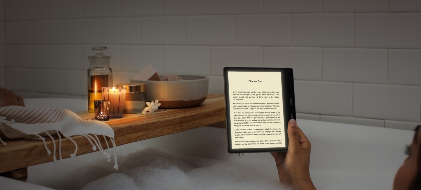 A woman reading an all-new Kindle Oasis in the bath by candle light