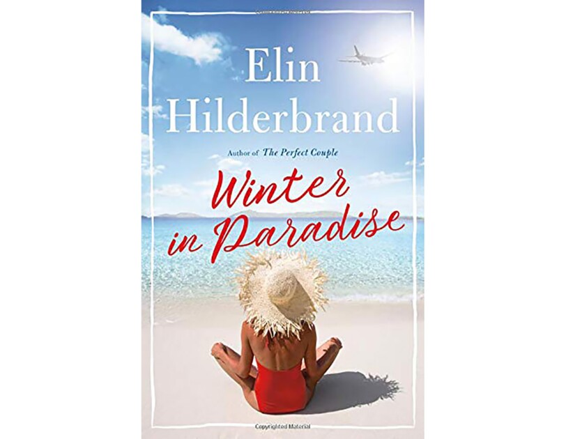 Book cover for "Winter in Paradise" by Elin Hilderbrand snows a tanned woman in a red halter one-piece swim suit and straw sitting cross legged on the beach, looking out toward the ocean.
