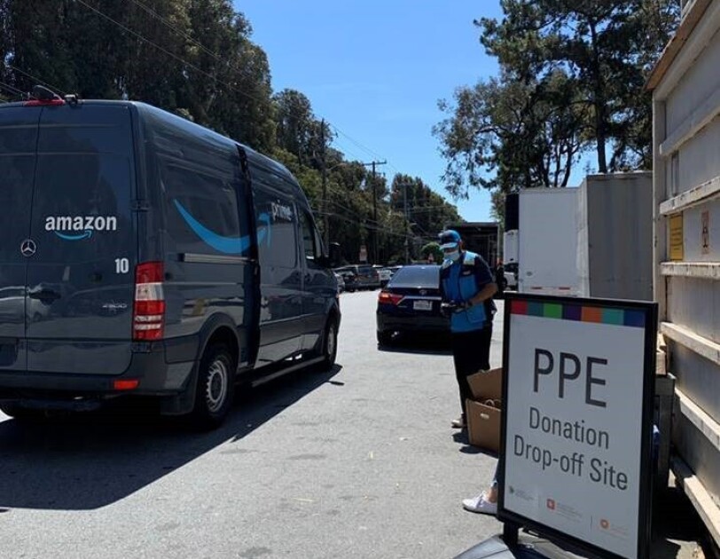 An Amazon delivery driver and van next to a sign that says "PPE Donation Drop-off Site."
