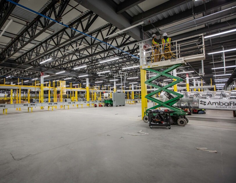 A crew works at building an Amazon Fulfillment center or warehouse in Cleveland, Ohio. Two men stand on a raised platform as they work on the ceiling