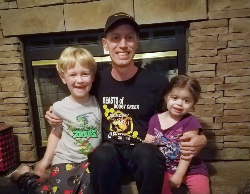 A man sits in front of a fireplace with two small kids.