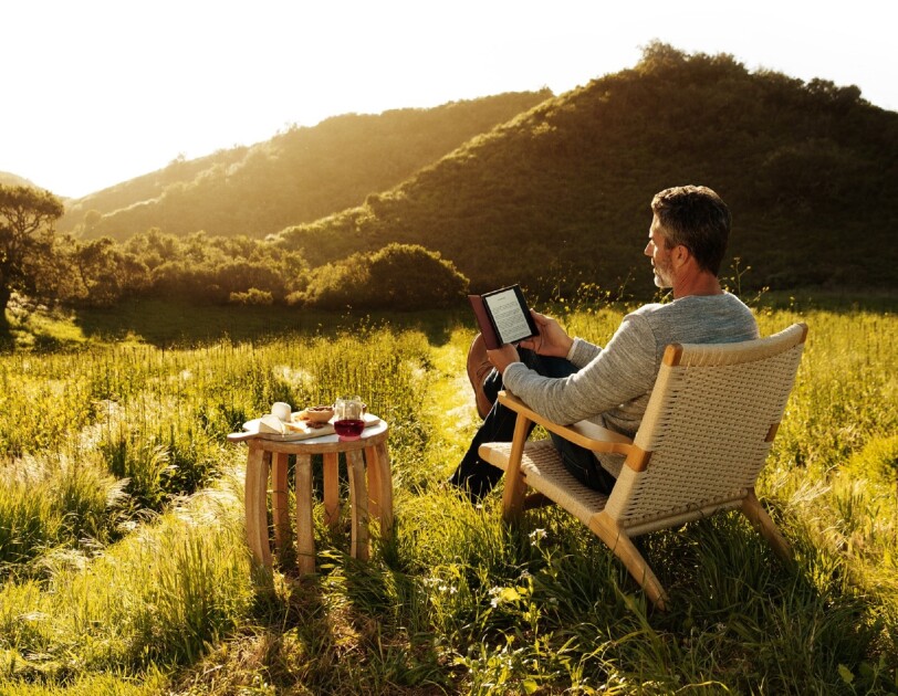 A man reading his all-new Kindle Oasis while looking out at the sun setting over a vineyard