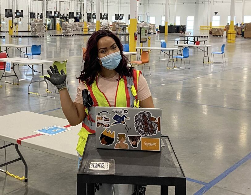 A woman wearing a safety vest and a mask works at a laptop computer.