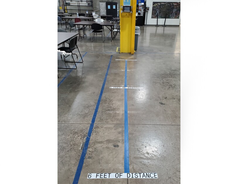A time clock at an Amazon fulfillment center, with marks on the floor showing where associates should stand while using, and where 6 feet of distance is from the time clock.