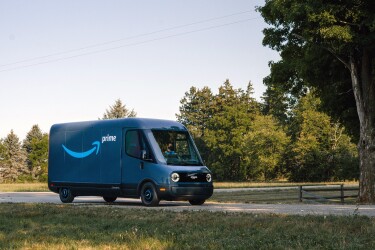 Furgone elettrico Rivian in una strada di campagna. Il furgone è blu e sulla fiancata ha il logo smile di Amazon e la scritta 'Prime'
