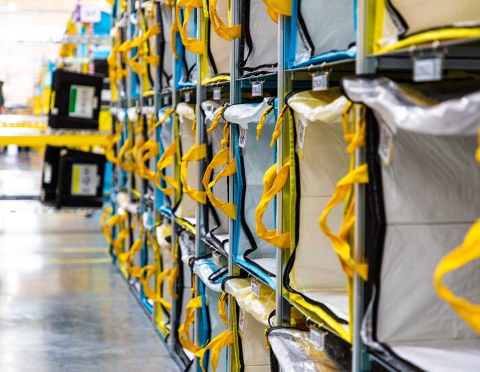 Estantería de un centro logístico con bolsas que tienen las asas de color amarillo. Las estanterías tienen cuatro pisos y más de 10 bolsas.