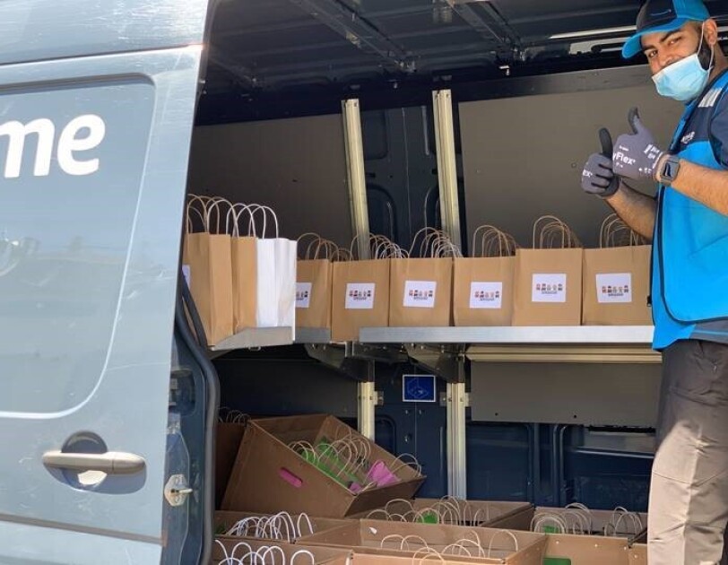 A delivery driver gives a thumbs-up sign while standing in a van filled with bags to be delivered.
