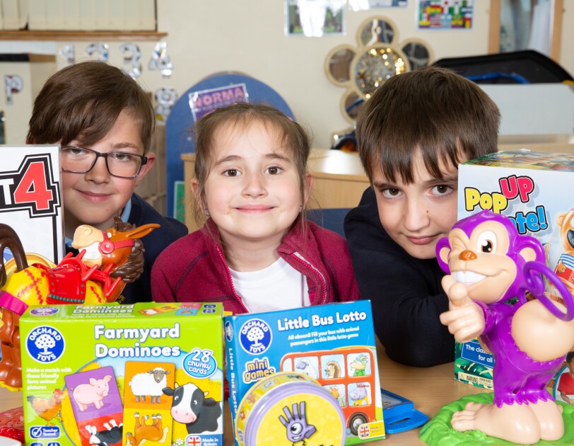 Three School children sitting behind a table full of colourful game boxes.