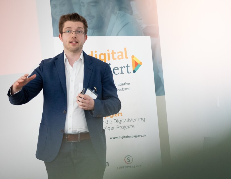 Daniel Stark steht vor einem digital.engagiert-Poster und gestikuliert