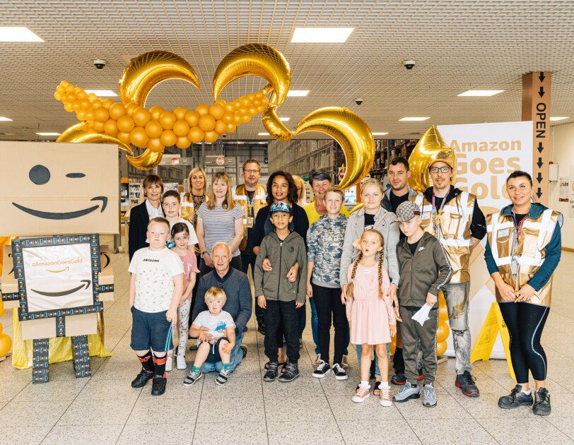 Amazon Goes Gold: golden decorations, children and Amazon employees with golden vests inside an Amazon fulfilment centre