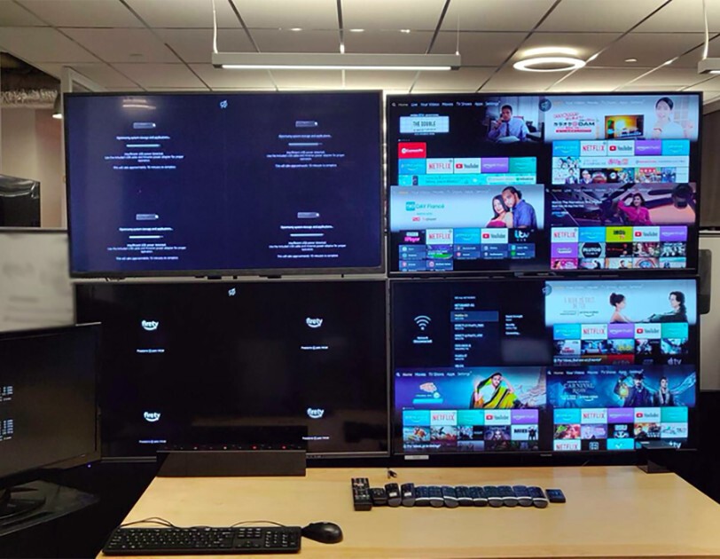 4 monitors in a work space, with a row of remotes and keyboard in front of them.