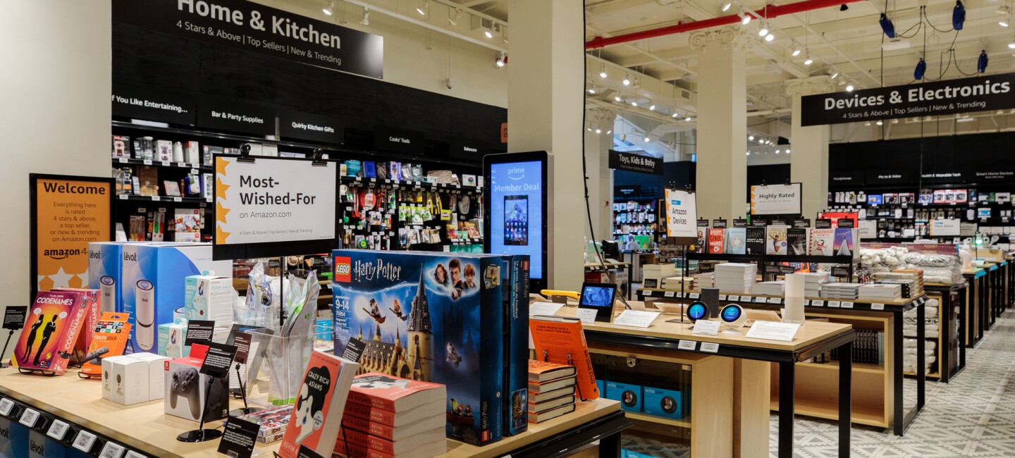 The view inside Amazon 4-star store. Tables are stacked with books, toys, devices, kitchen implements, and cookbooks.  "Home & Kitchen," "Devices & Electronics," and Toys, Kids & Baby section signage is visible.