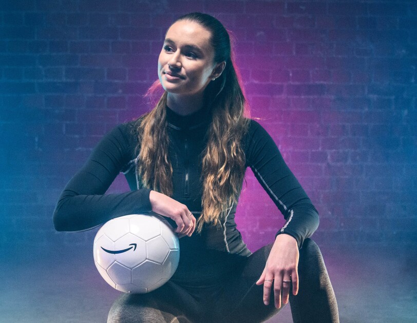 Lia Lewis crouching in a hall with a football which has the Amazon Smile logo