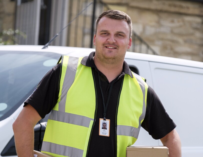 JMHC delivery driver holding Amazon packages in front of a delivery lorry