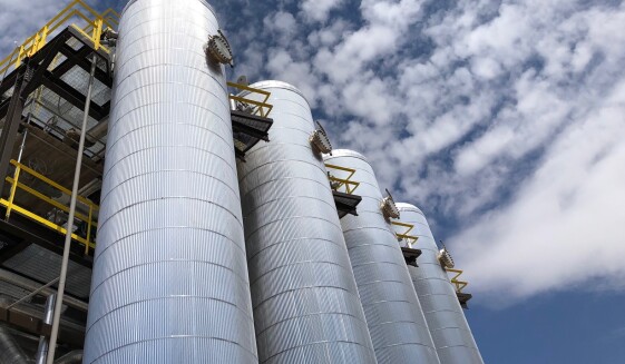 Four metal cylindrical structures shown against a blue sky with clouds.