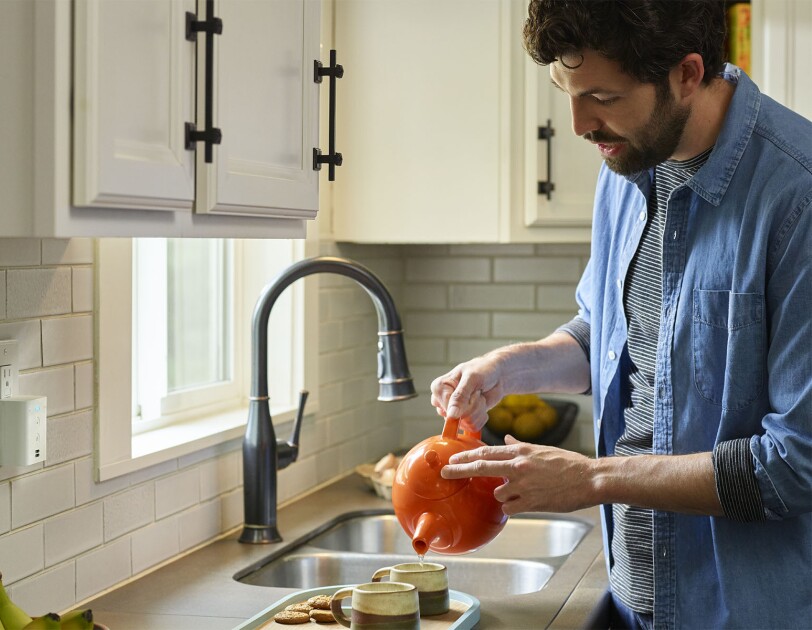 Amazon Echo Flex device in a kitchen, near where a man prepares a cup of tea.