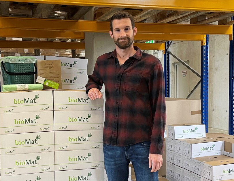Ein Mann in einem karrierten Hemd steht neben einem STapel voller bioMat Verpackungen.