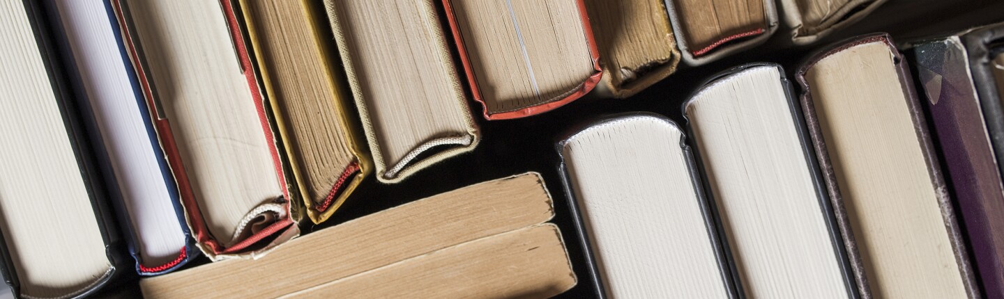 Many hardbound books stacked tightly together at various angles, seen edge on.