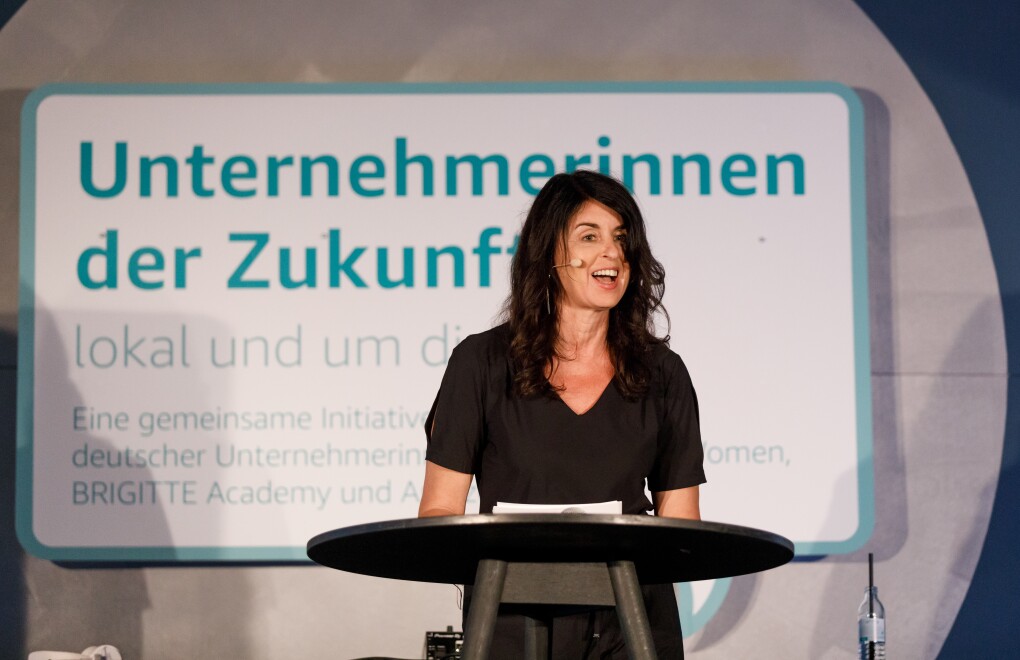 Brigitte Huber steht auf de Bühne am Rednerpult, sie hält eine Laudatio und verkündet die Gewinnerin
