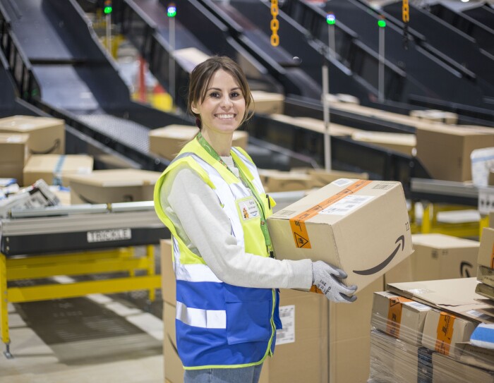 Piano americano di Ilaria di Bartolomeo, Operations Manager di Amazon a Casirate (Bergamo), mentre lavora nel centro di smistamento. Sorregge in mano un pacco con il sorriso di Amazon.