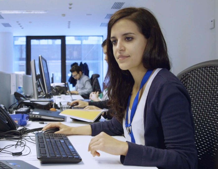 Ritratto di Nadia Cazzamali, Account Manager Marketplace di Amazon. E' seduta alla sua scrivania e guarda a uno dei due schermi che ha di fronte. Sullo sfondo, alla sua destra, due suoi colleghi e le finestre dell'ufficio.