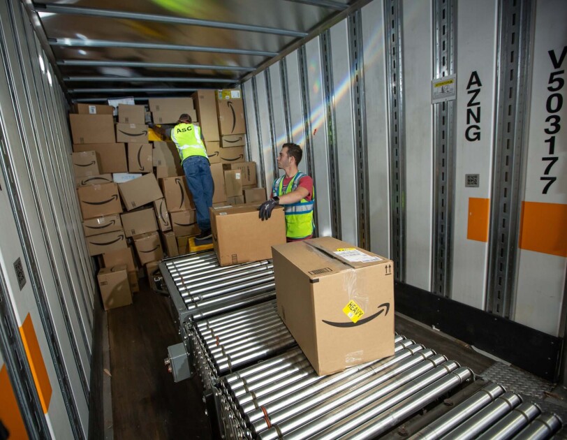 Two Amazon associates receive packages from a conveyor belt, as they prepare to place them on a trailer for distribution at a Columbus, Ohio fulfillment center, CMH2