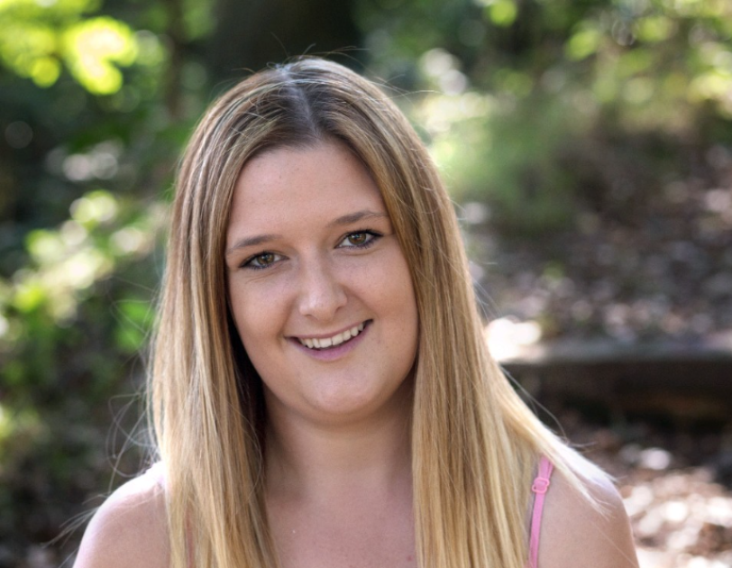 A headshot of Genna Holliss sitting in a woodland park.