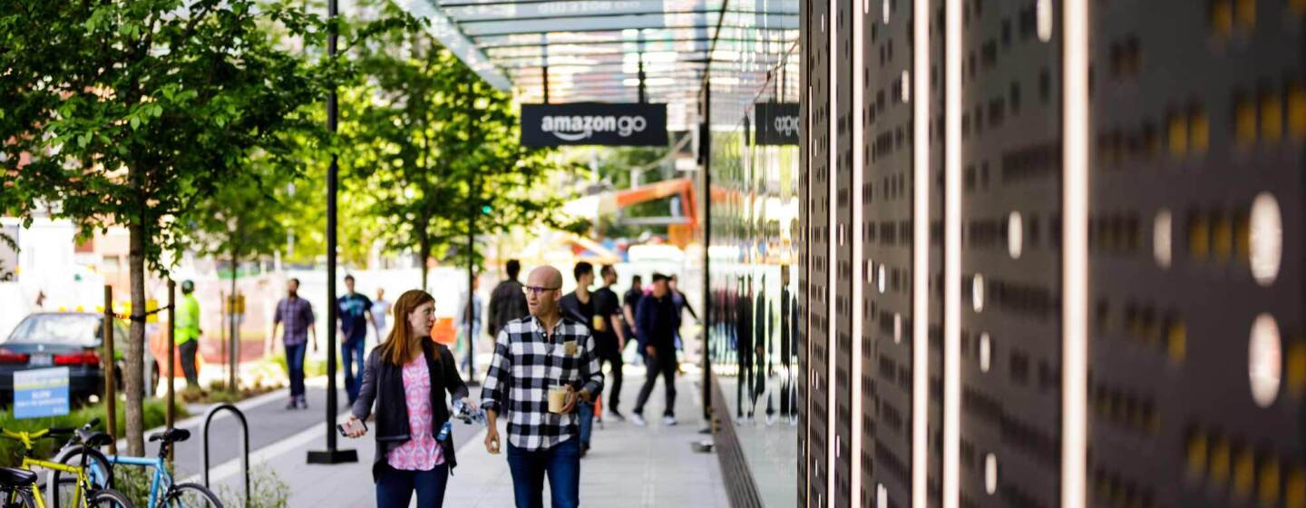 Amazon employees walk on the sidewalk past Amazon Go flagship store in Seattle, Washington