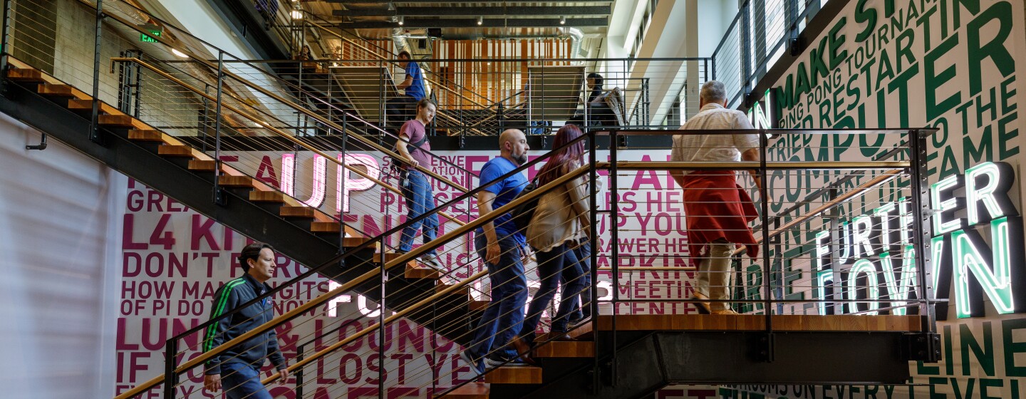 Amazon employees climb a set of stairs that are decorated with inspirational slogans, like "try something new".