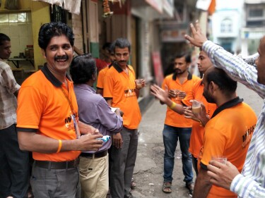 Amazon employees in orange shirts communicate with each other in sign language on a street in Mumbai, India.