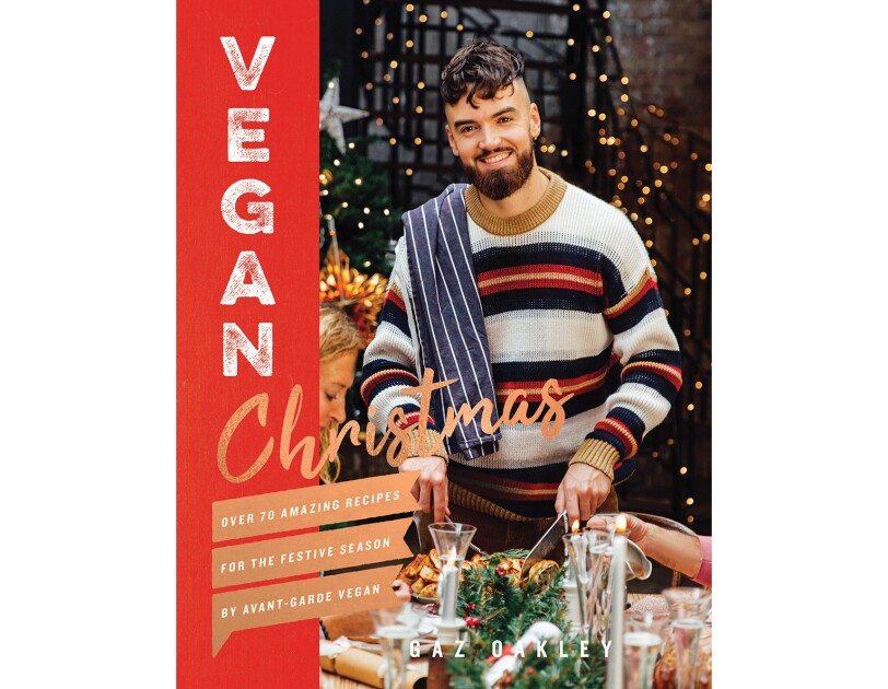 Vegan Christmas cookbook features a man wearing a sweater, with a dish towel thrown over his shoulder, carving into a dish. On either side of him are guests at his table, appearing to enjoy a holiday meal.