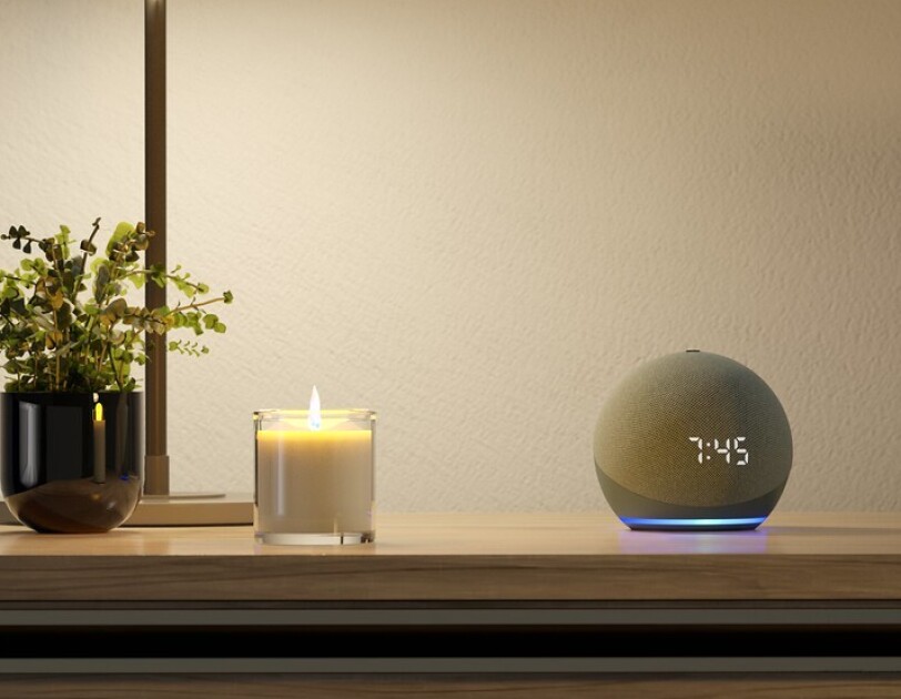 An Amazon Echo Dot on a nightstand next to a candle, a plant and a lamp.