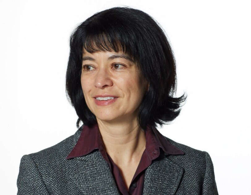 A headshot of Jacqui Chin wearing a greay blazer and looking to the left.