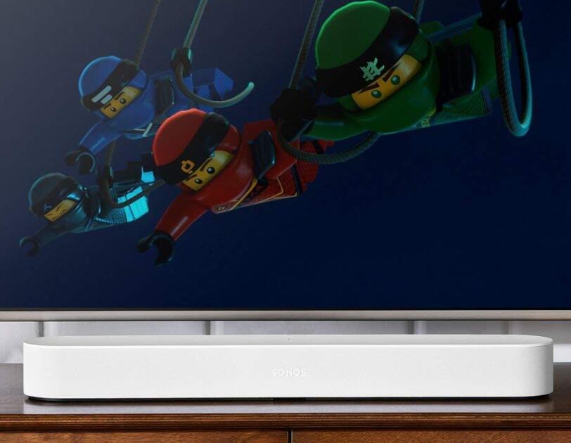 A television screen shows The Lego Movie, below the tv screen is a white Sonos Beam device. Both items sit on a television stand.