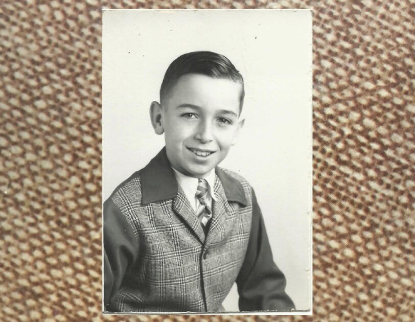 Rick Reefer at age 10. It's a black and white photograph and he is smiling and wearing a tweed jacket.