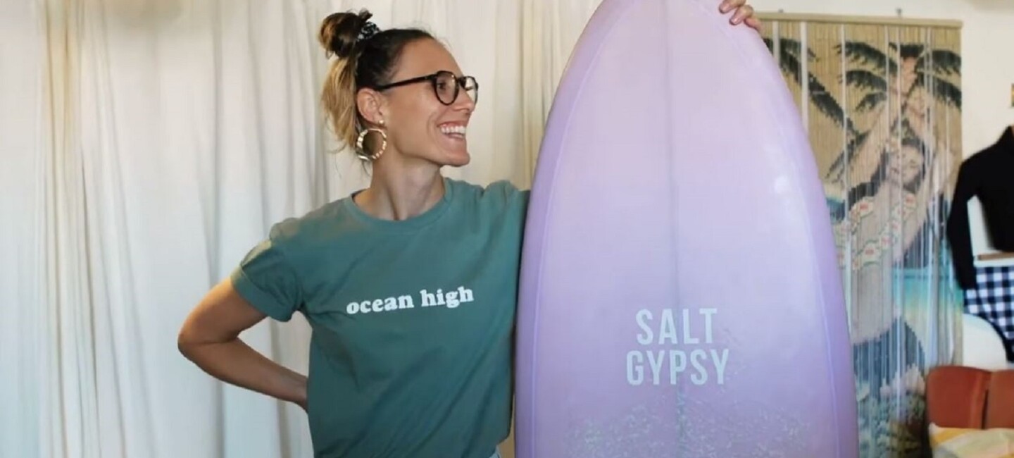 Salt Gypsy’s founder Danielle Clayton holding a surfboard in her shop