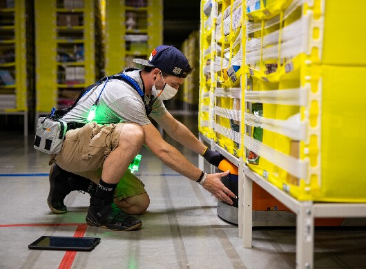 An Amazon employee works on a robot in an FC while wearing a safety vest