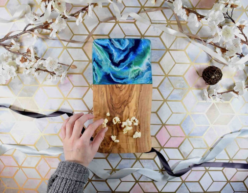 Birds-eye view of someone picking up popcorn from a Kate Chesters Resin Board, There are decorative flowers and ribbons surrounding the board.