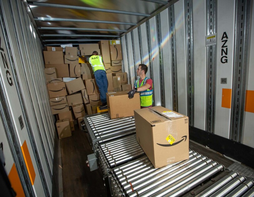 Two Amazon associates receive packages from a conveyor belt, as they prepare to place them on a trailer for distribution at a Columbus, Ohio fulfillment center, CMH2