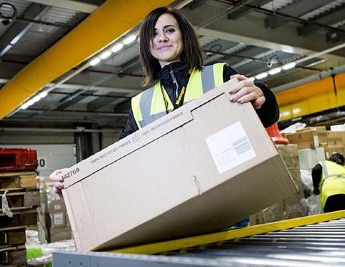 Amazon Mitarbeiterin stehe am Fließband und hat einen Karton in der Hand.