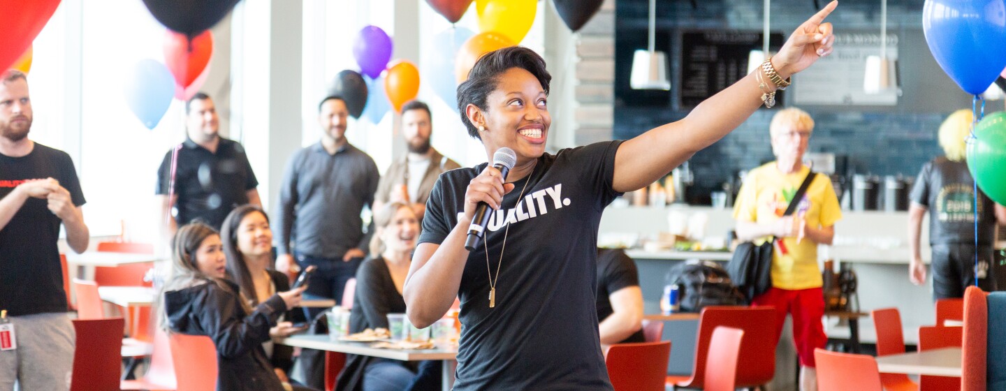 A woman Amazonian in a black t-shirt that says Equality points during a speech.